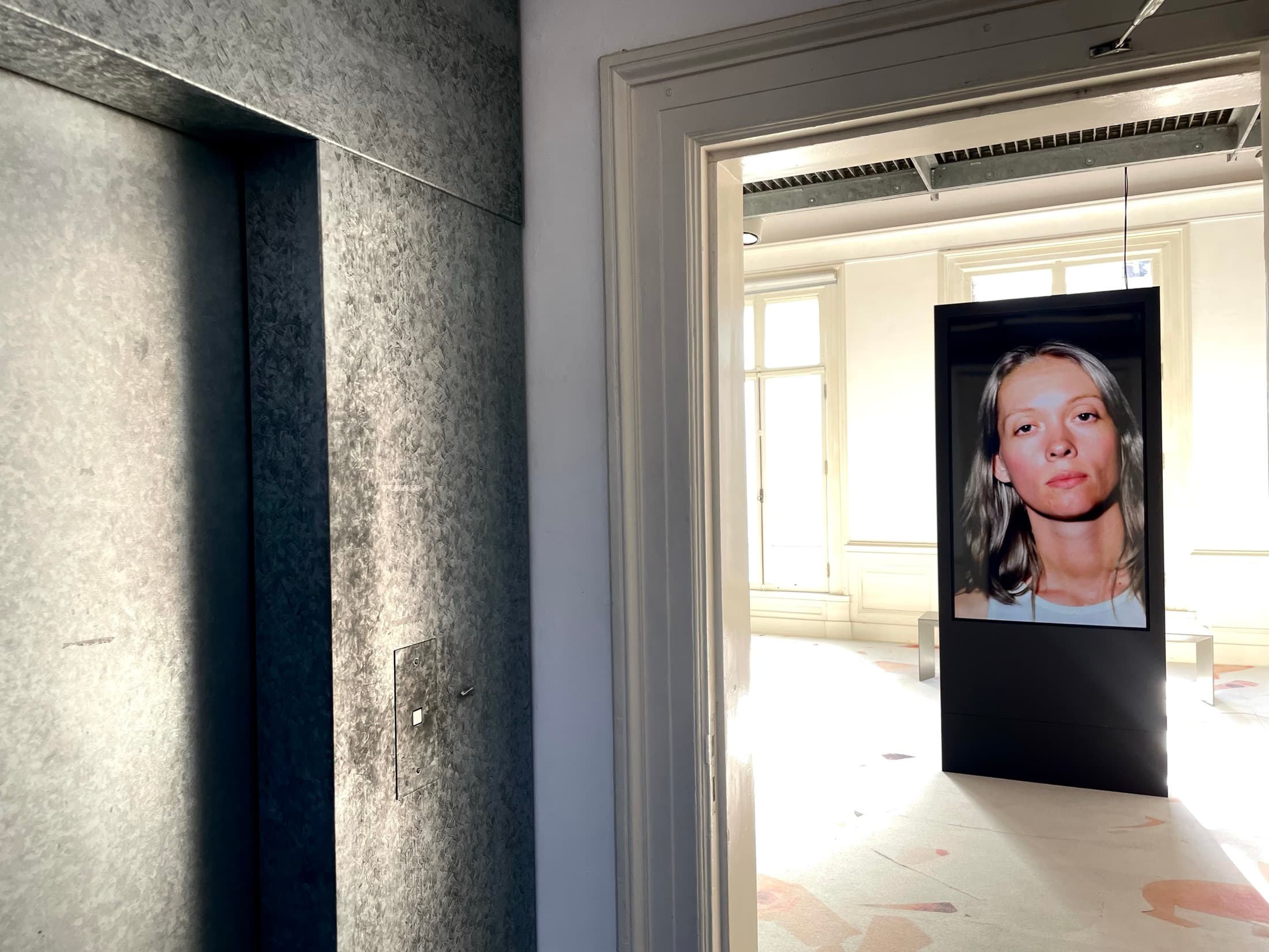 A tall printed portrait hanging in a bright corridor