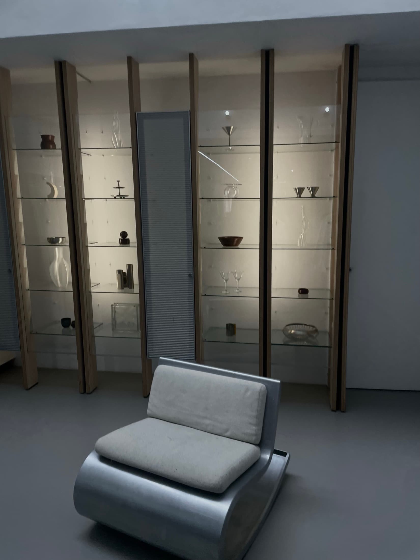 Lit glass cabinets of glassware and ceramics behind a low aluminium chair