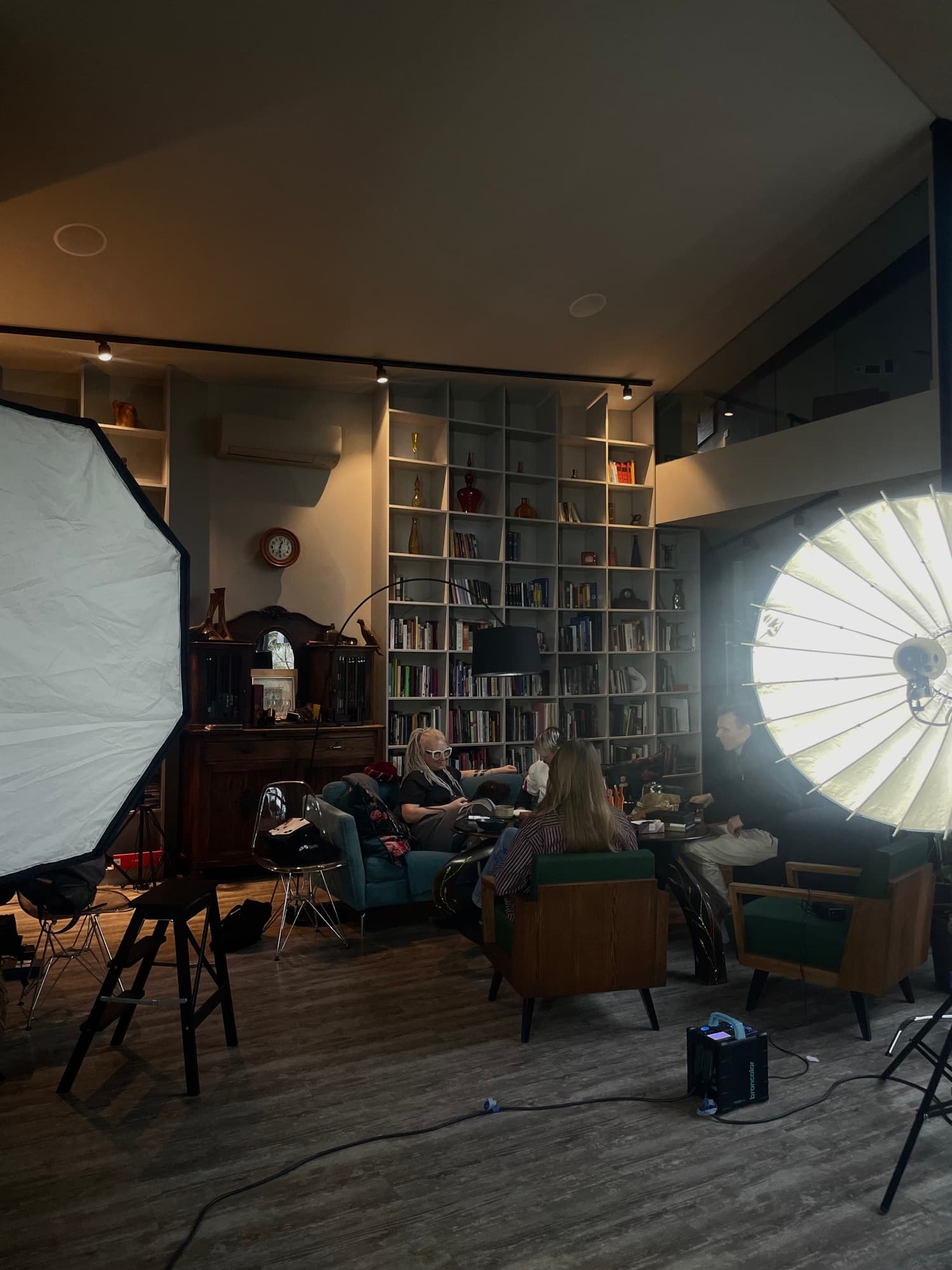 A shoot set up in a book-lined room, a large softbox on one side and a parabolic light on the other